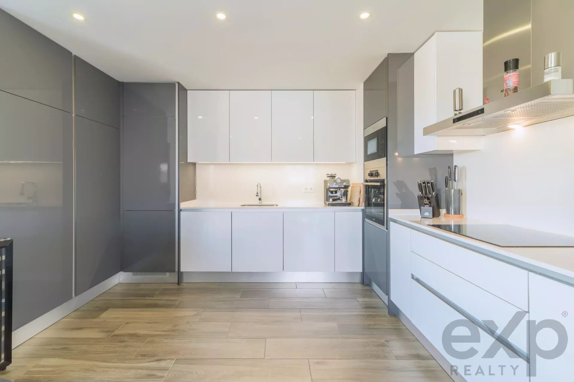 Modern, handleless gray and white kitchen with built‑in fridge, wall cabinets, and stainless steel oven area on the right.