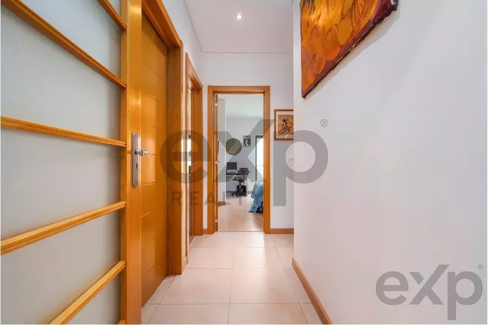 Bright interior hallway with tiled floor, frosted glass panel on the left, and wooden doors; a workspace is visible at the end.