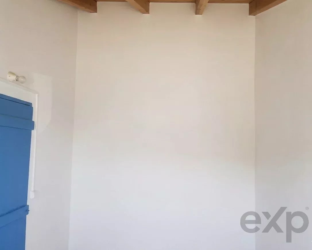 Interior corner of a room with white walls, exposed wooden ceiling beams, and a blue door on the left side.