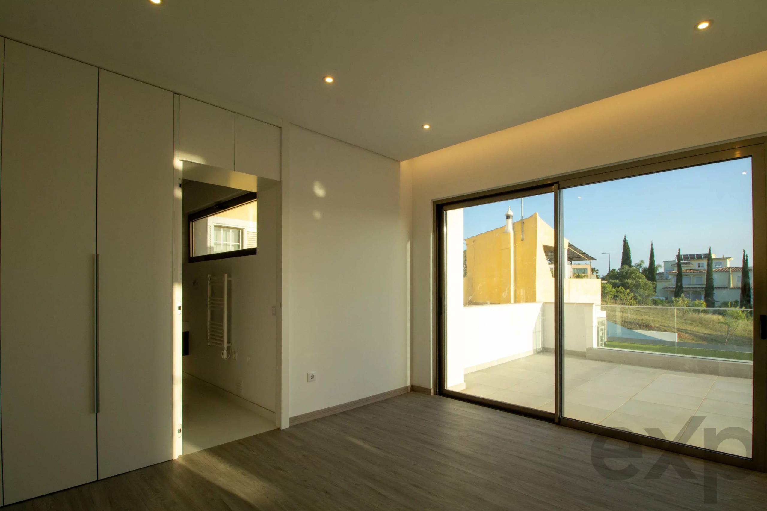 Modern living space with built-in cabinets on the left and large sliding glass doors to a balcony, daytime exterior view.