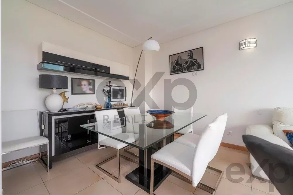 Modern dining room with glass tabletop, four white upholstered chairs, and a sideboard against a white wall.