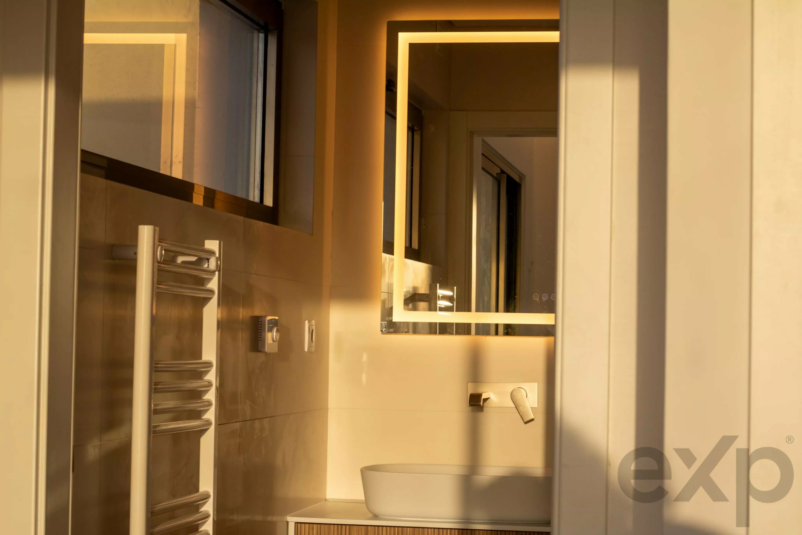 Modern bathroom featuring a backlit rectangular mirror, warm lighting, beige walls, and a white vessel sink on a wooden vanity.