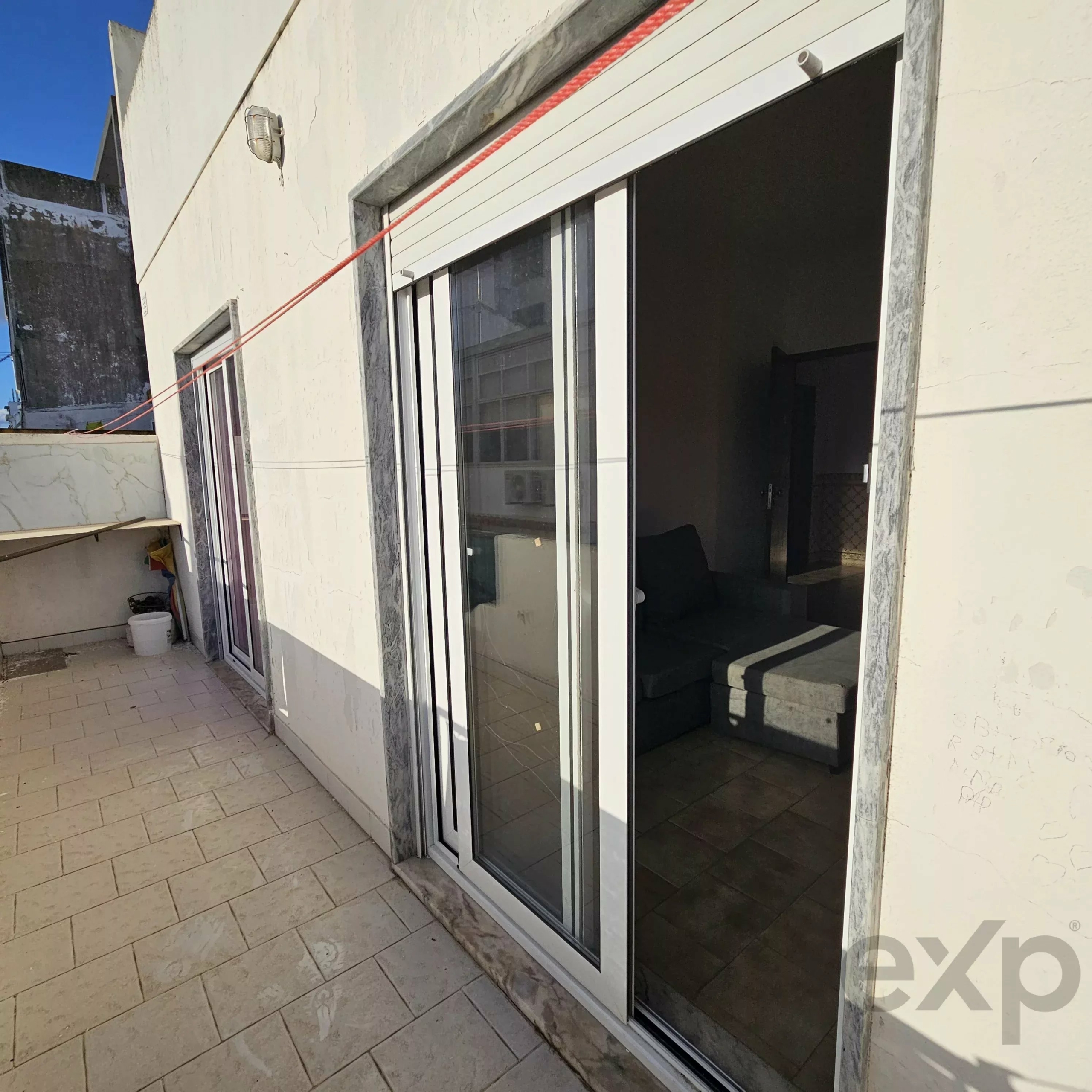Exterior scene of white building with large sliding glass doors and marble trim, blue sky, and a string line across the doorway.