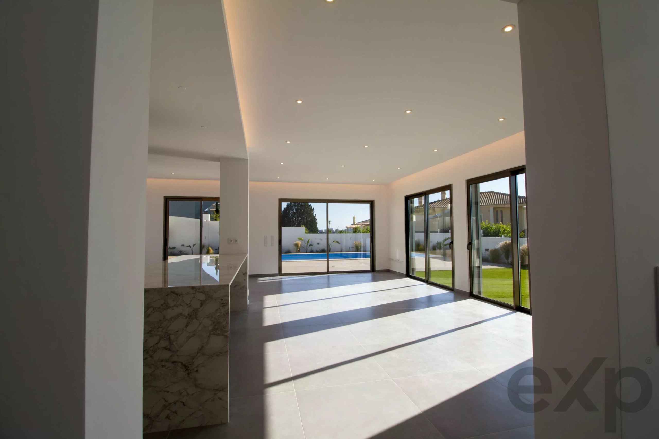 Bright, modern open-plan interior with large glass doors opening to a pool and lawn outside.