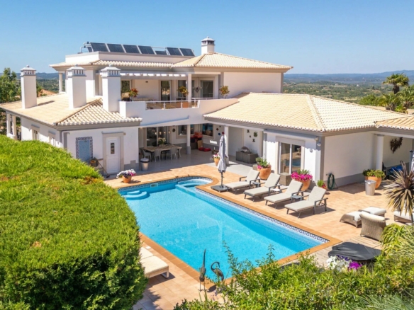 White Mediterranean villa with a terracotta roof, poolside loungers, and hillside views.
