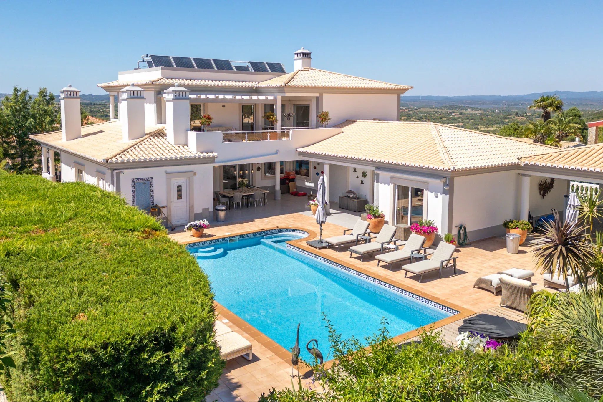 White Mediterranean villa with a terracotta roof, poolside loungers, and hillside views.