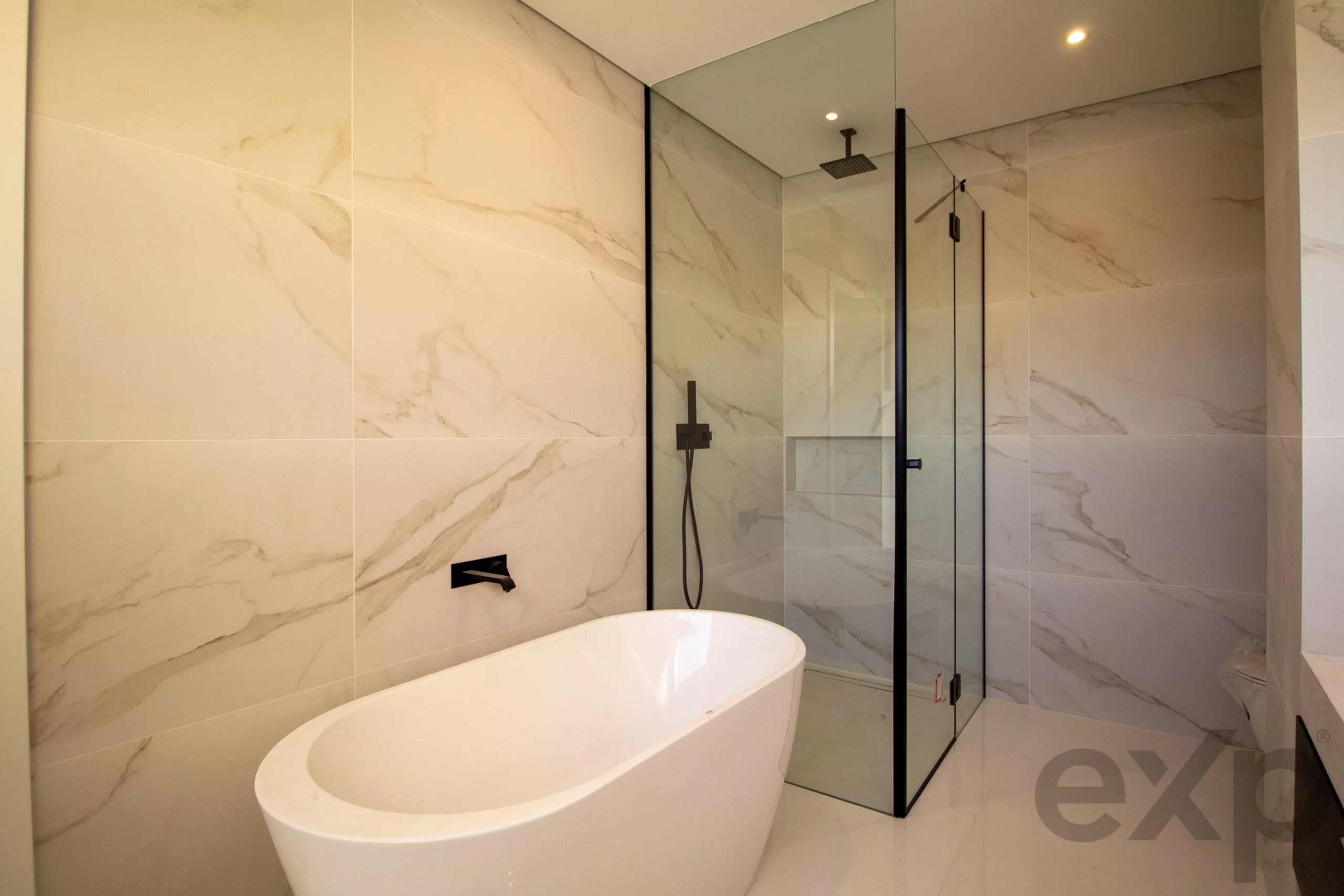 Modern bathroom with a white freestanding bathtub and glass-walled shower, marble walls and black fixtures.