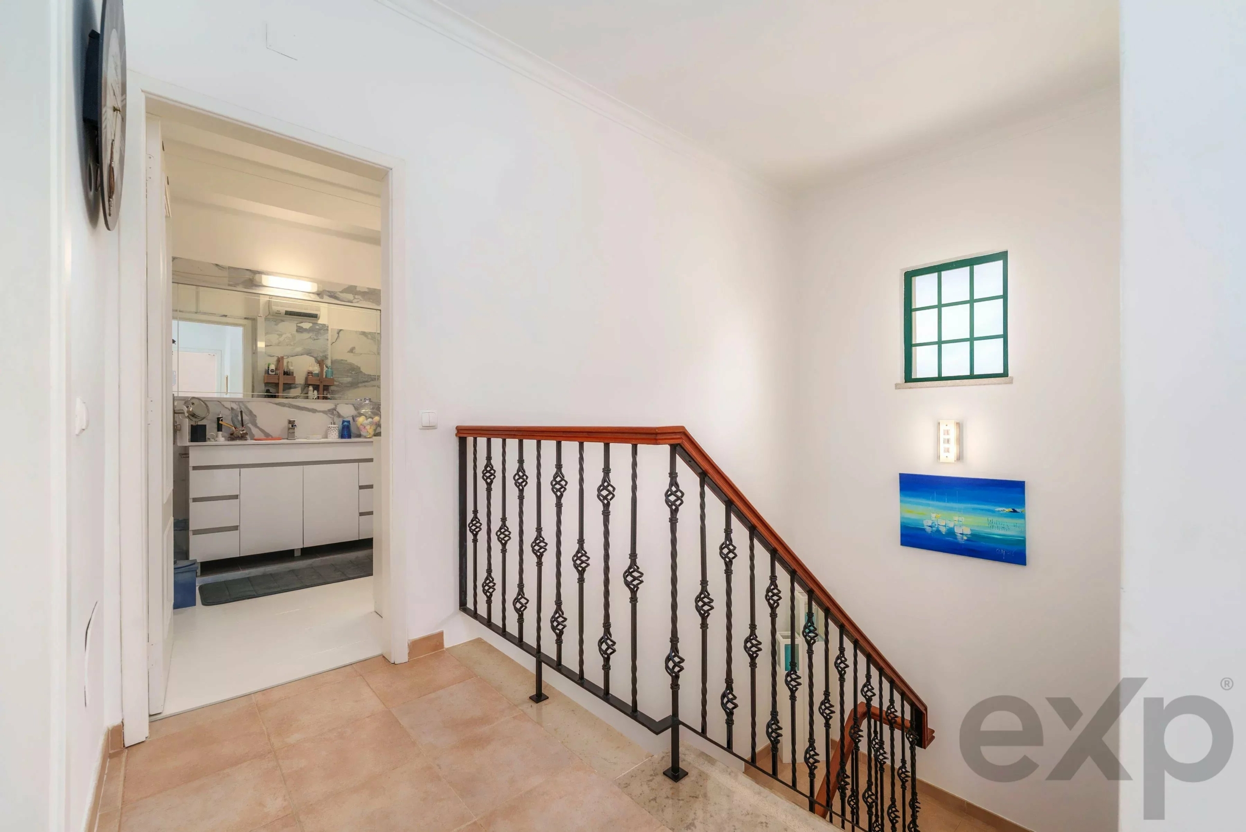 Bright stairwell with a decorative black railing and beige tiled floor; open doorway to a bright bathroom/kitchen area on the left.