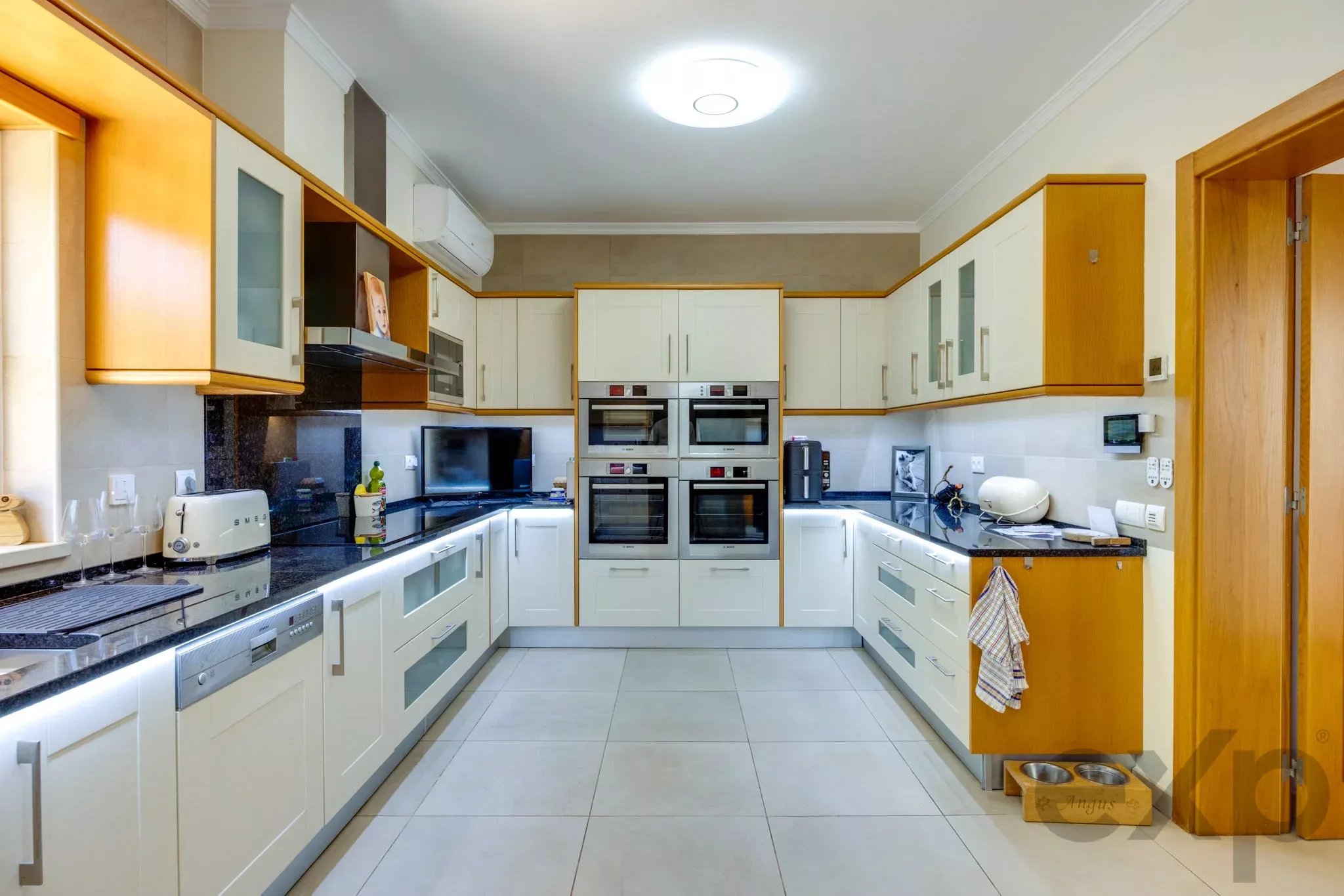 Bright, modern kitchen with white cabinets, dark granite counters, and wooden trim; double ovens centered on back wall.