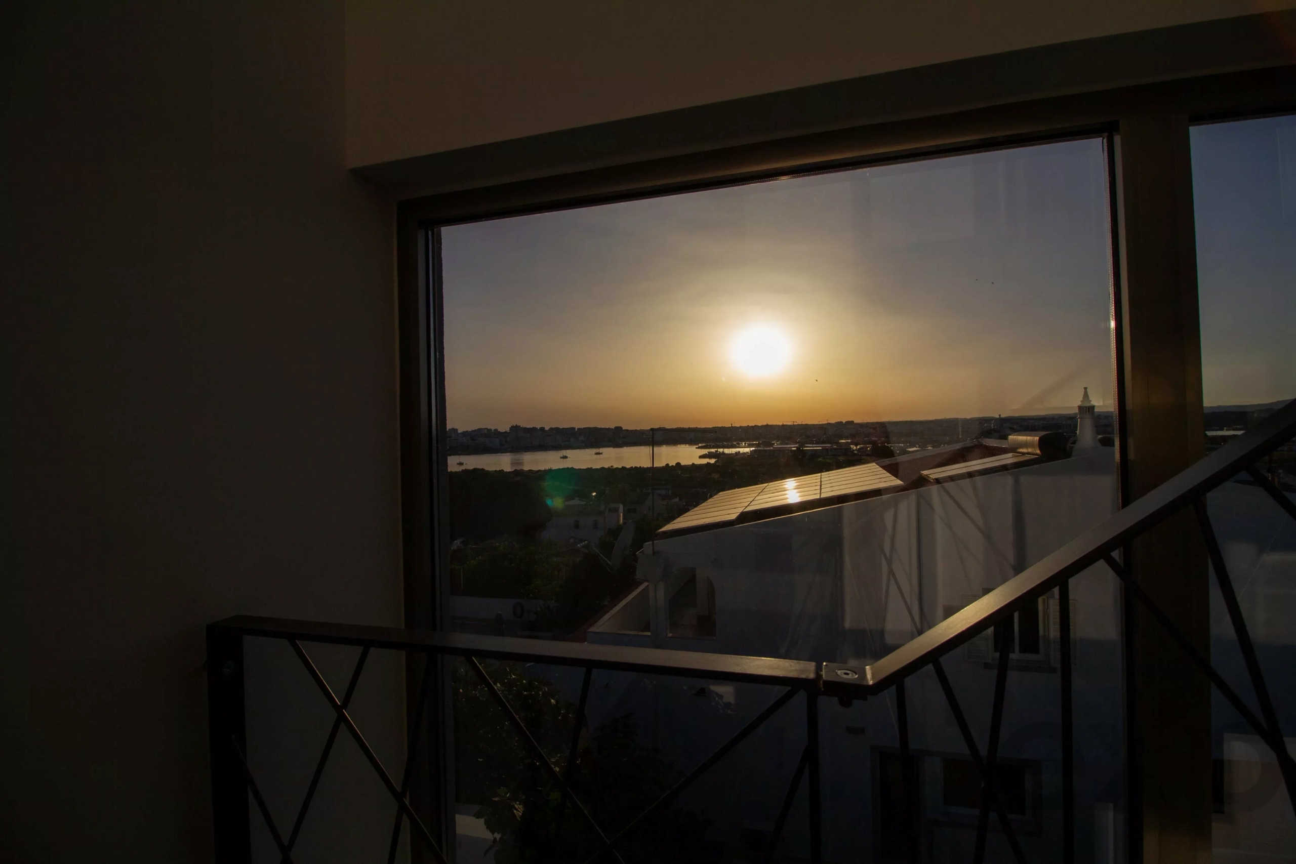 Sunset view through a large window, with an orange sky and distant skyline visible outside the glass door/window.