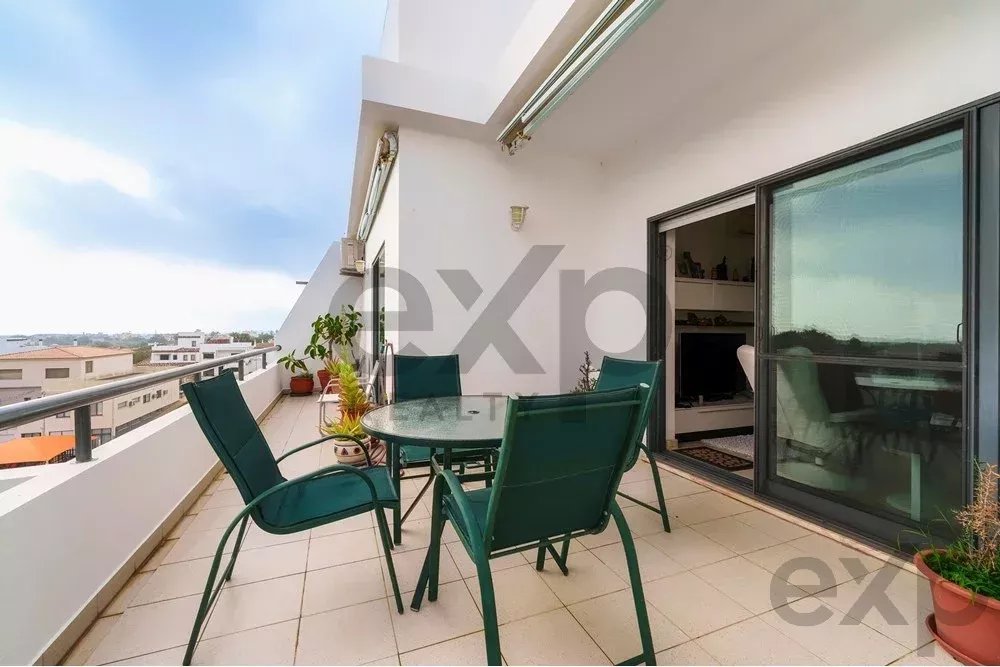 Balcony with a glass round table and four green chairs, overlooking a city skyline from a high-rise apartment.