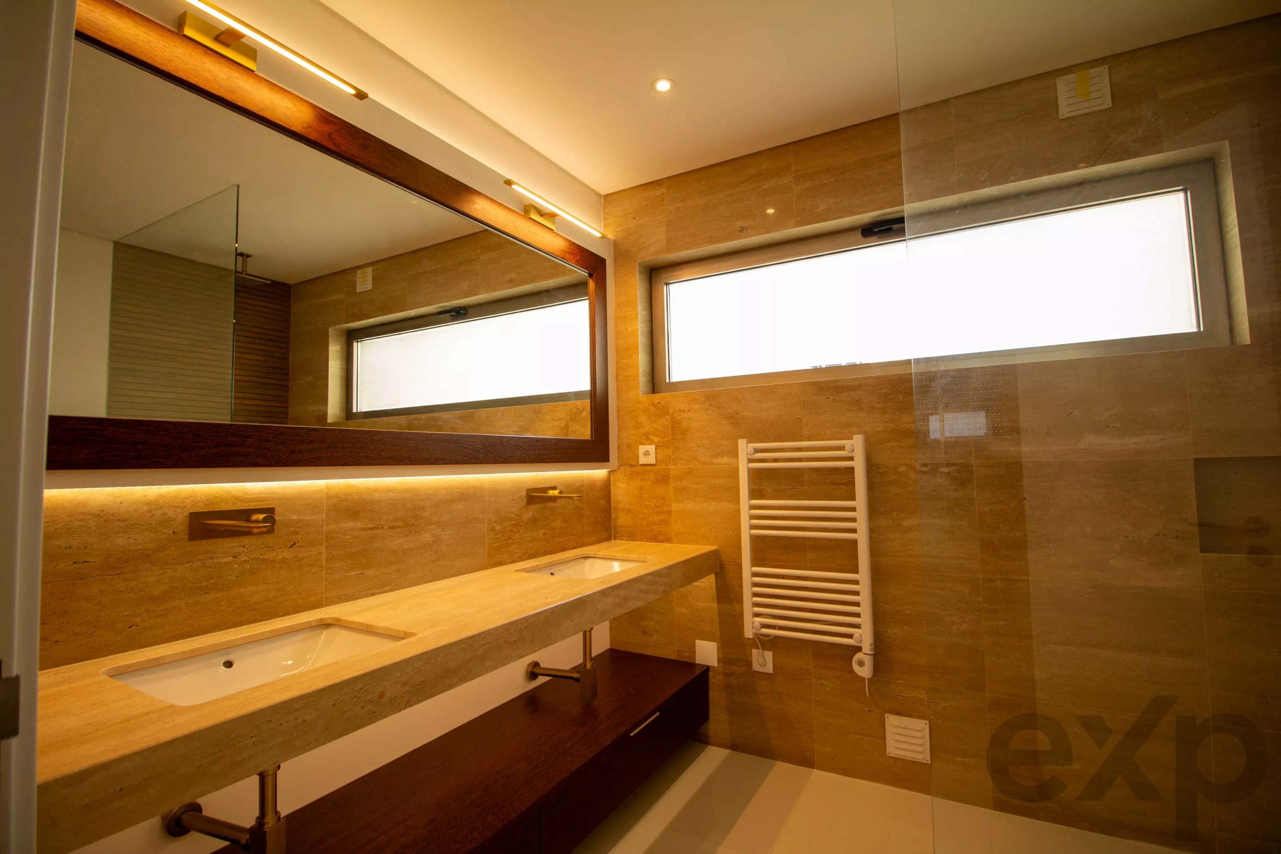 Modern bathroom with a long marble countertop sink, large mirror, and warm lighting