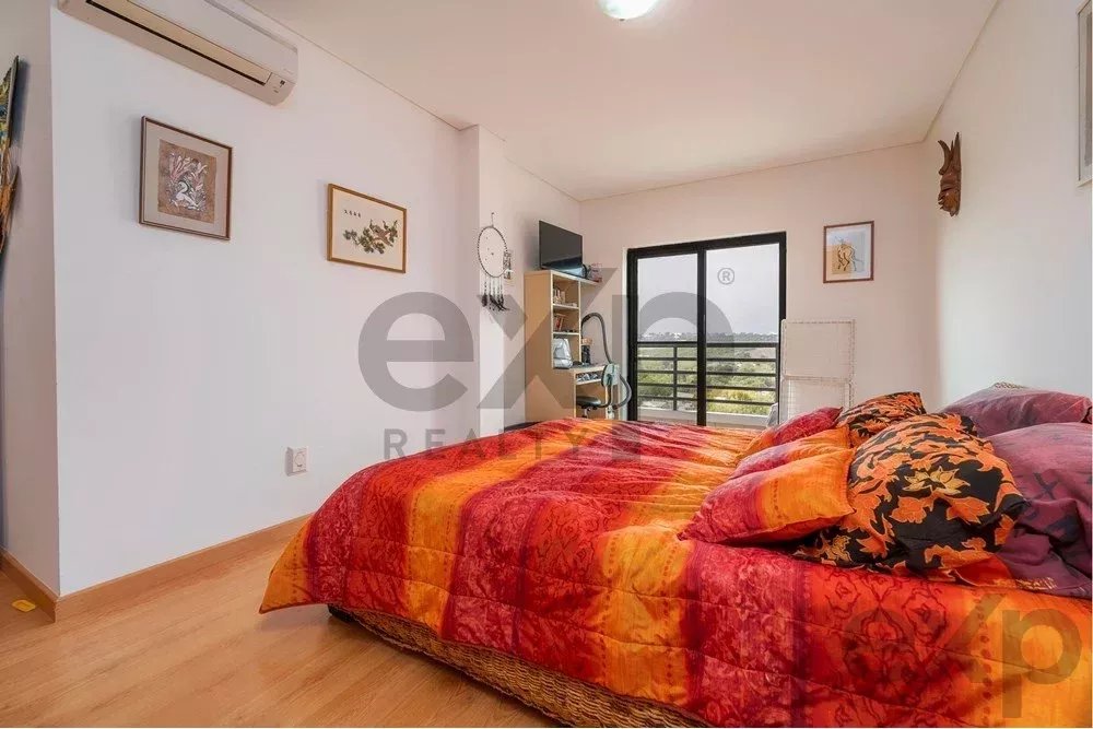 Bedroom with a vibrant red-orange quilt on a low bed, decorative pillows, and a balcony door letting in light.