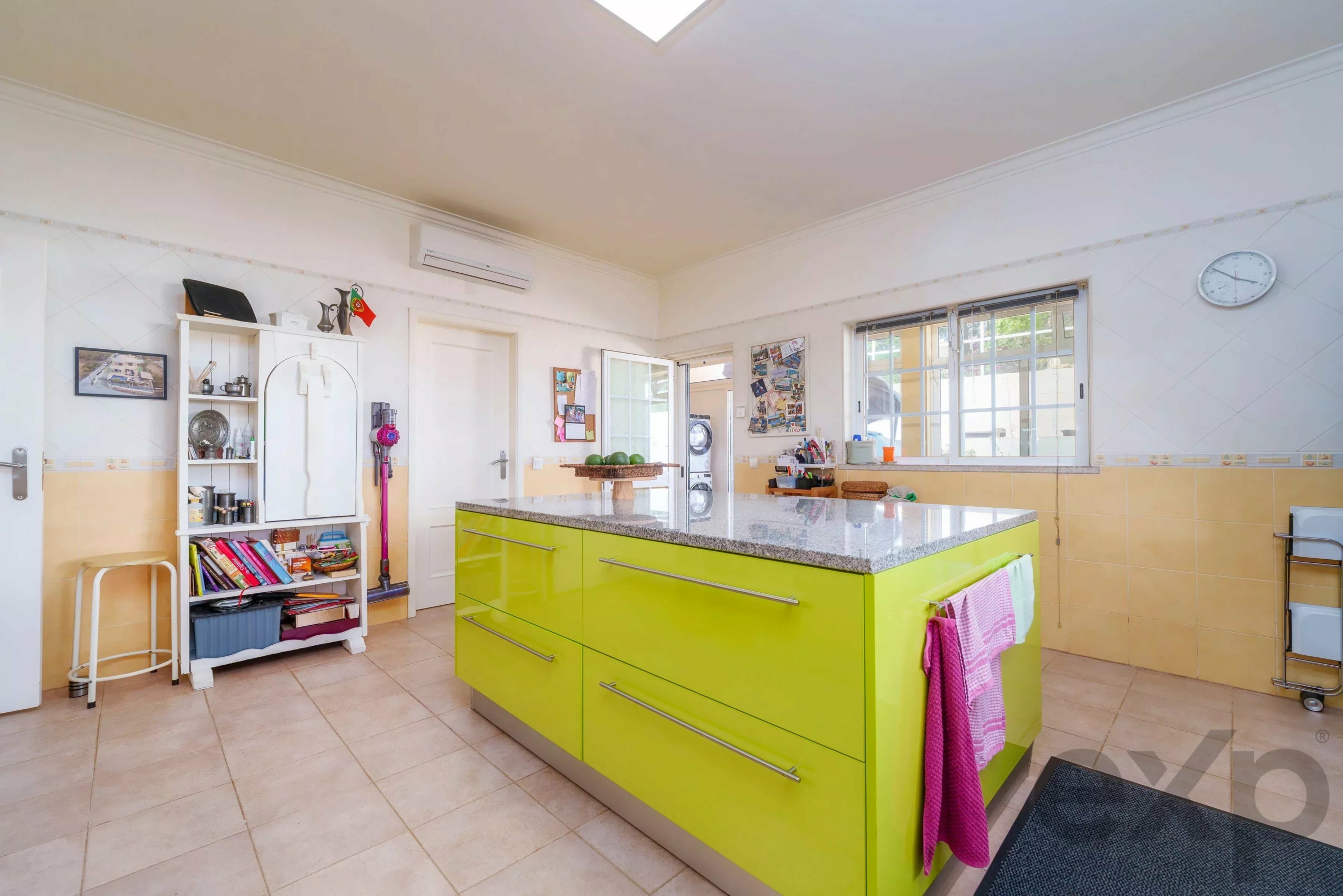 Bright, modern kitchen featuring a lime-green island with a granite countertop and white cabinets, large windows, and wall clock.
