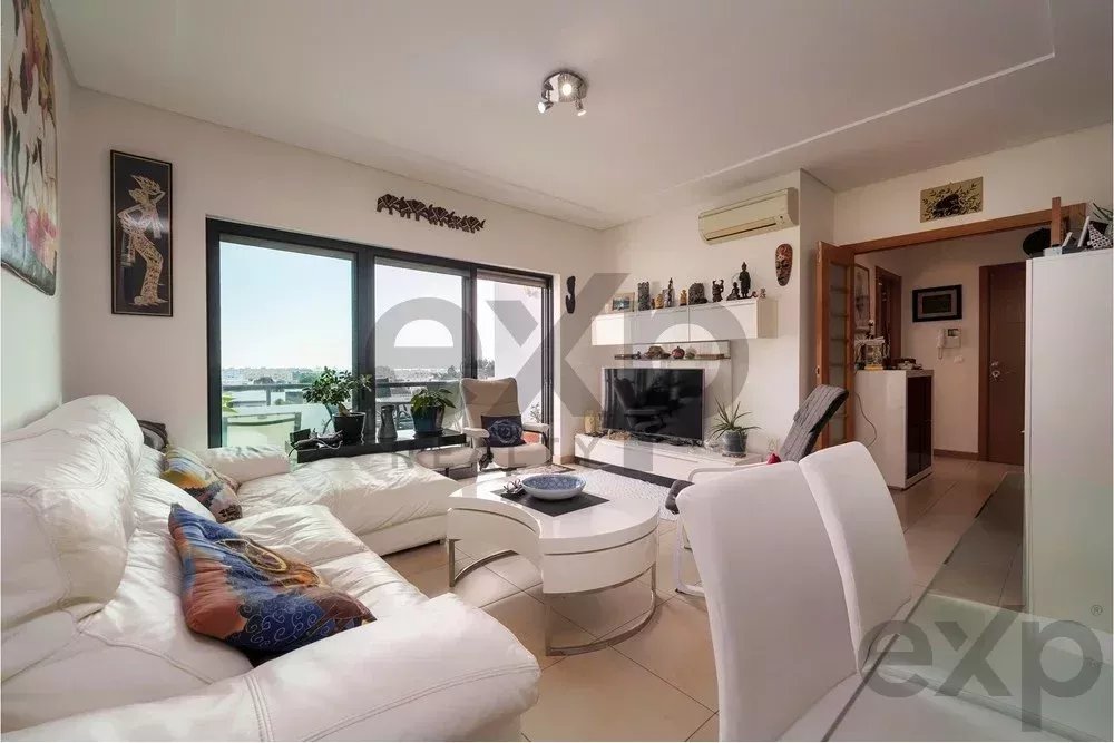 Bright living room with a white sectional sofa, round white coffee table, and large glass doors to a balcony.