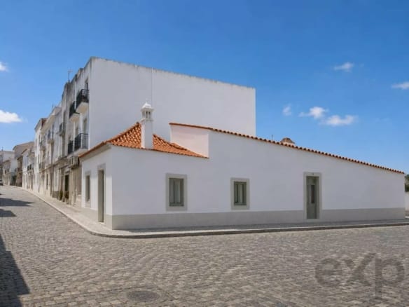 White-washed building with a red tile roof on a cobblestone street under a clear blue sky.