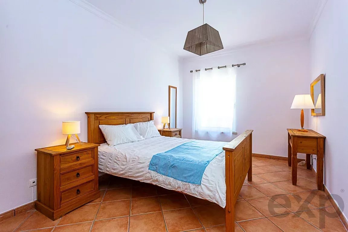 Wooden bedroom with a queen bed, two matching nightstands, and warm lamps on each side; white bedding with a blue throw.