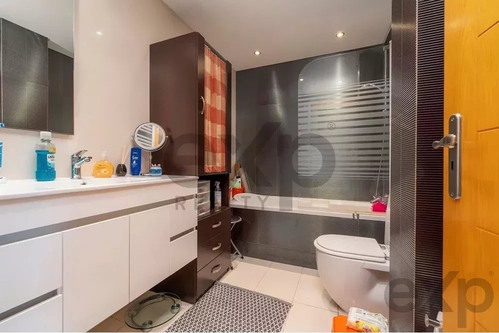 Modern bathroom with a white vanity, chrome fixtures, and a tub behind a frosted glass panel.