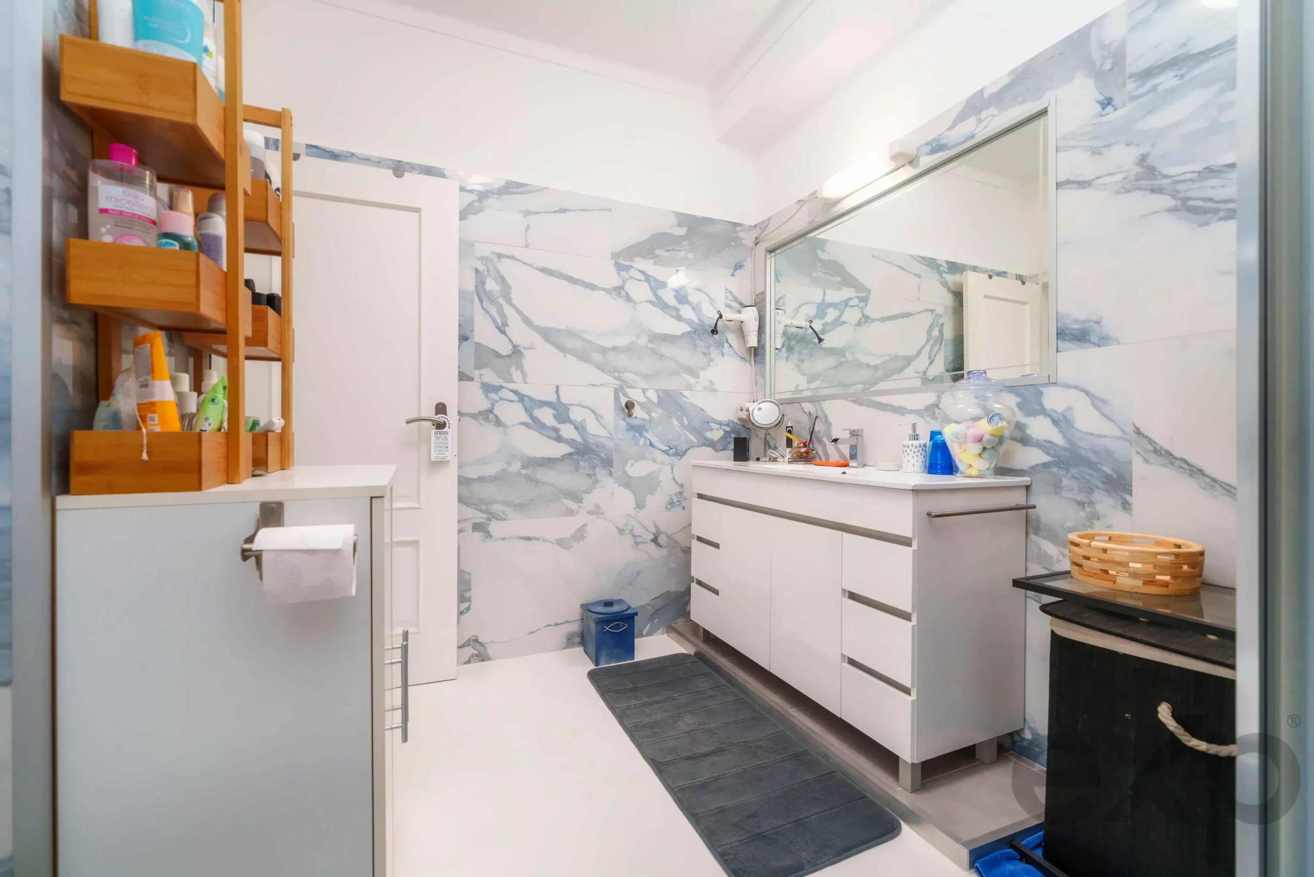 Bright bathroom with white vanity, marble-patterned walls, and a large mirror above the sink.