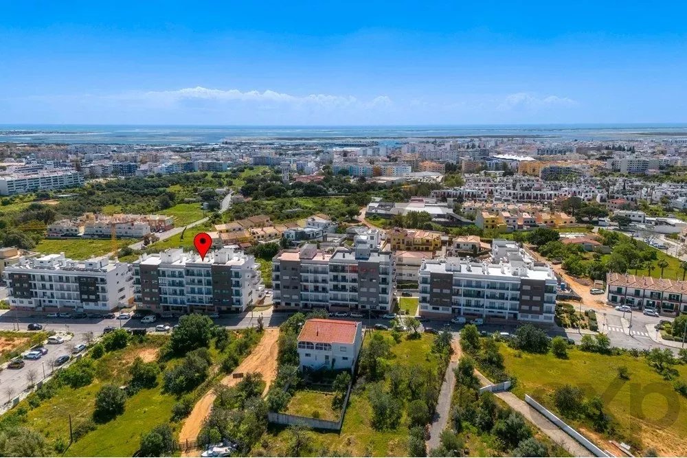 Aerial view of a coastal town with modern apartment buildings; red map pin marks a middle building in the foreground