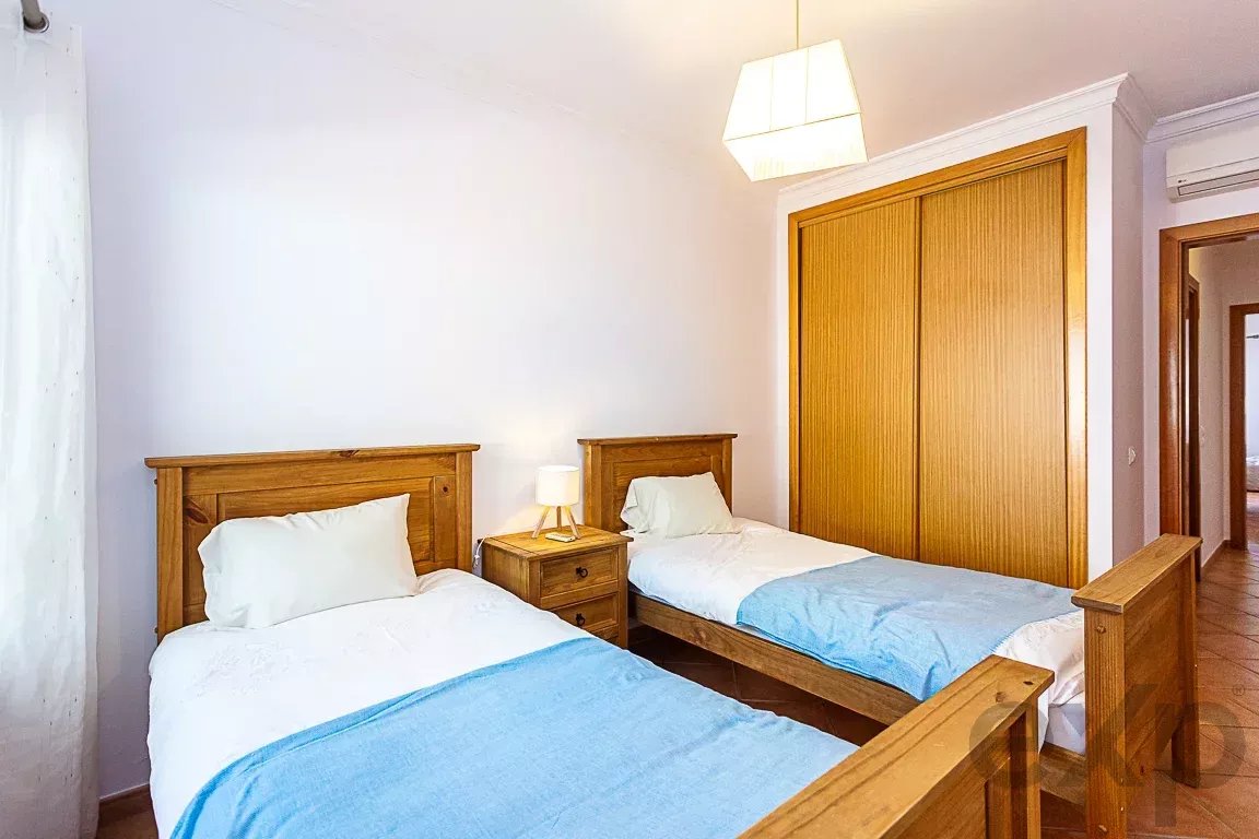 Twin beds with wooden frames and light blue bedding in a bright bedroom, with a nightstand and lamp between them.