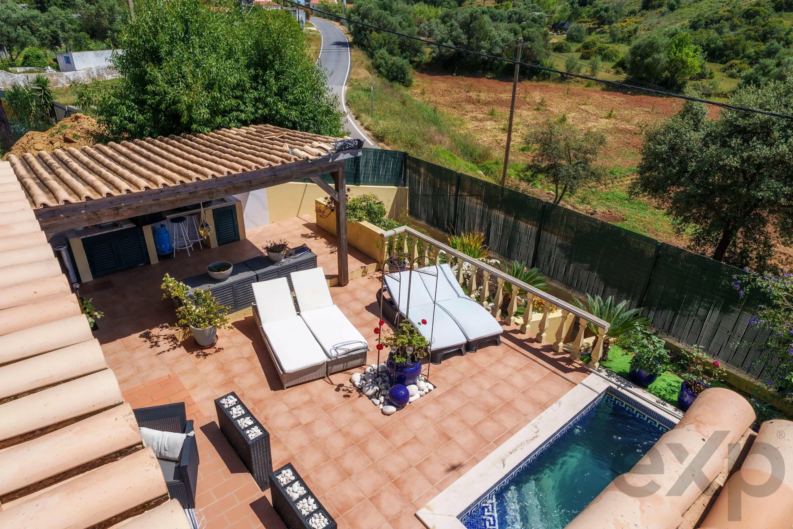 Terrace with lounge chairs by a rectangular pool, potted plants, and a tiled patio overlooking rural hills.