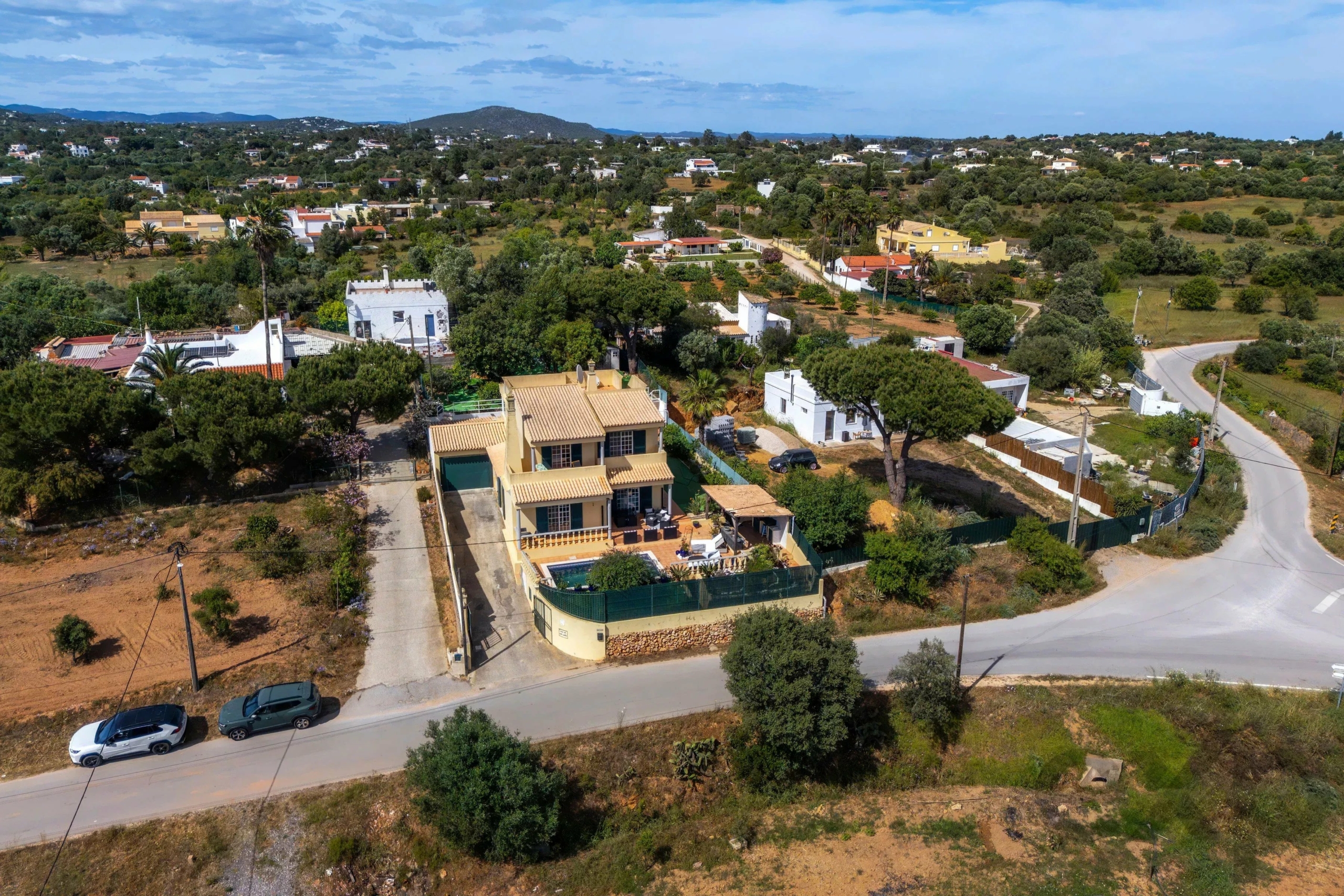 Aerial view of a suburban neighborhood with houses, trees, and winding streets under a blue sky.