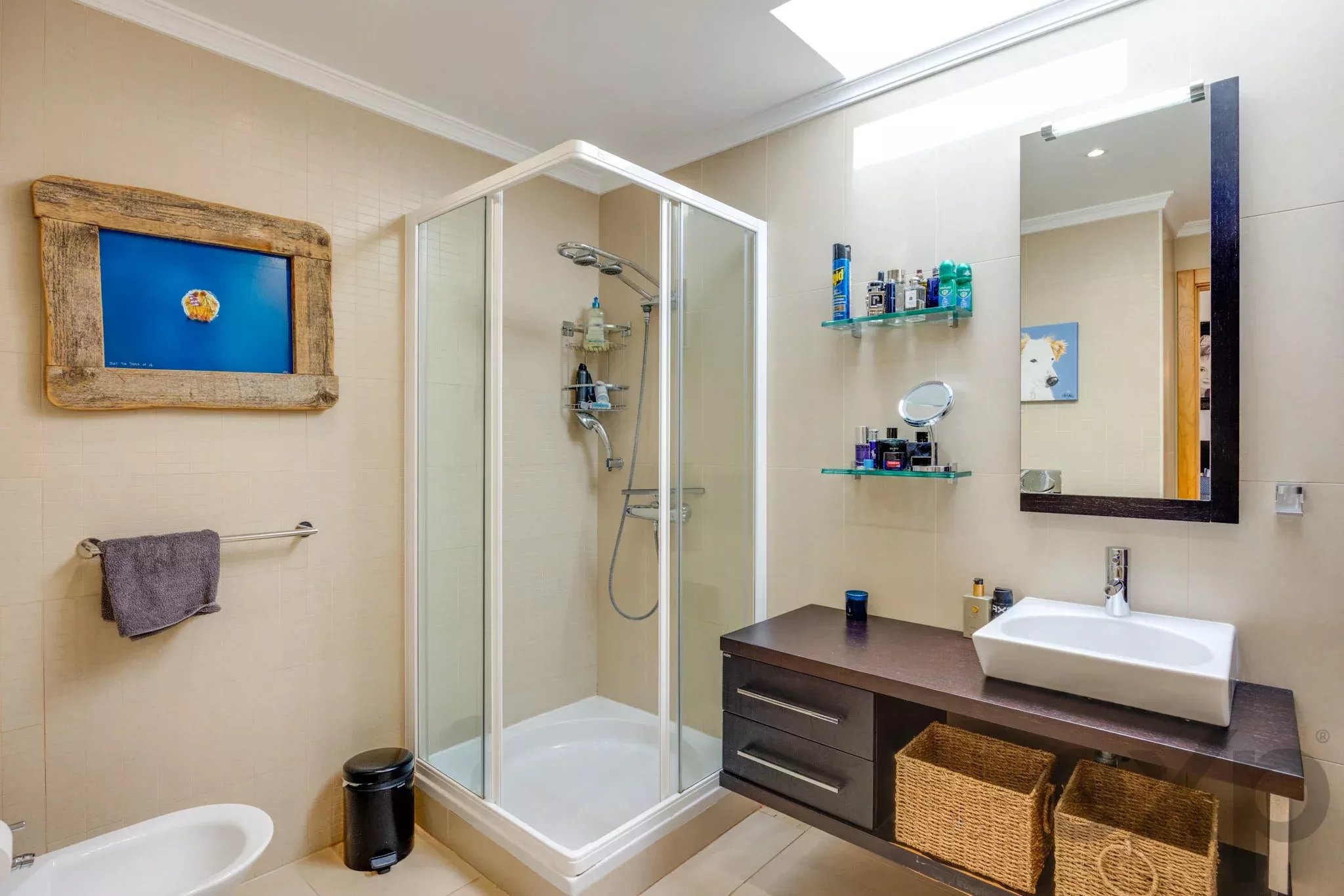 Modern bathroom with glass shower enclosure, dark wood vanity, white rectangular sink, and wicker baskets under the counter.