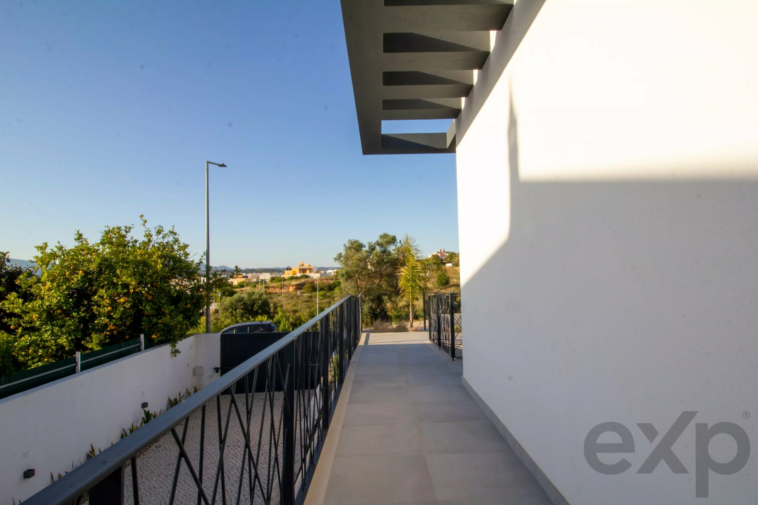 Outdoor walkway beside a white building, with a black metal railing and angular gray overhangs against a clear blue sky.