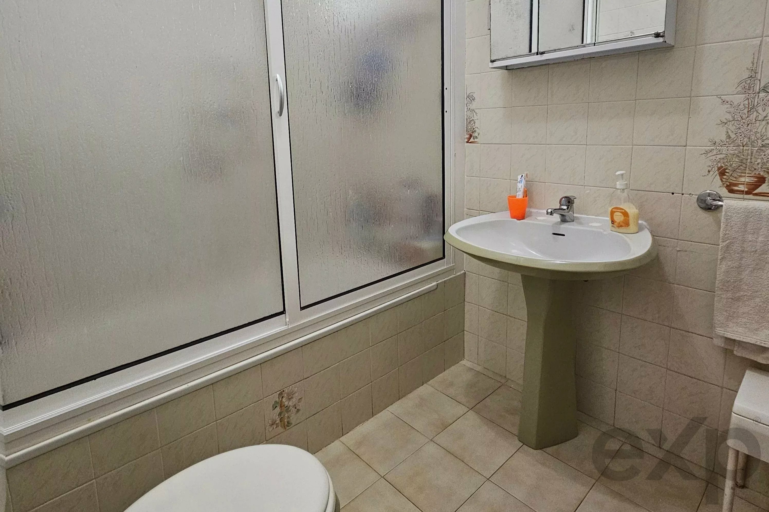 Bathroom with frosted glass shower enclosure, pedestal sink, and towel rack on tiled walls.