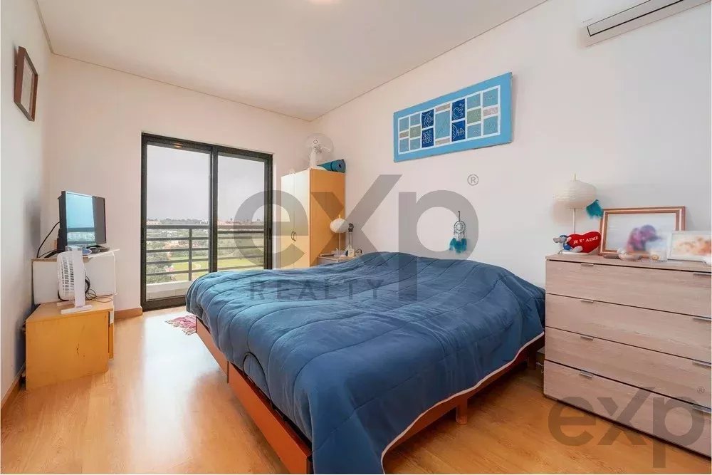 Bedroom with a blue-queen quilt on a low bed, sliding balcony doors, and a dresser on the right.