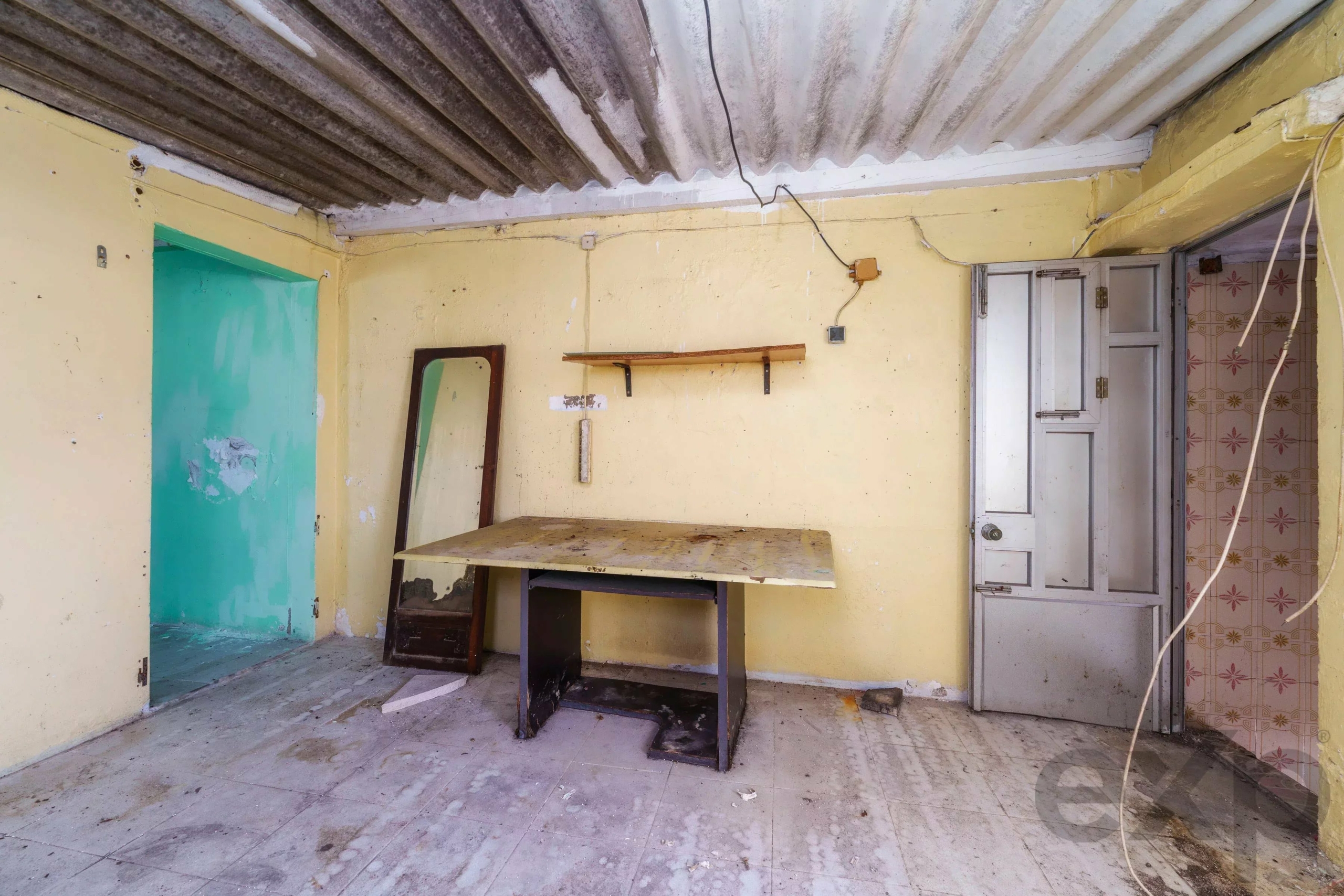 Abandoned yellow-walled workshop with a weathered wooden workbench and a leaning mirror against the wall