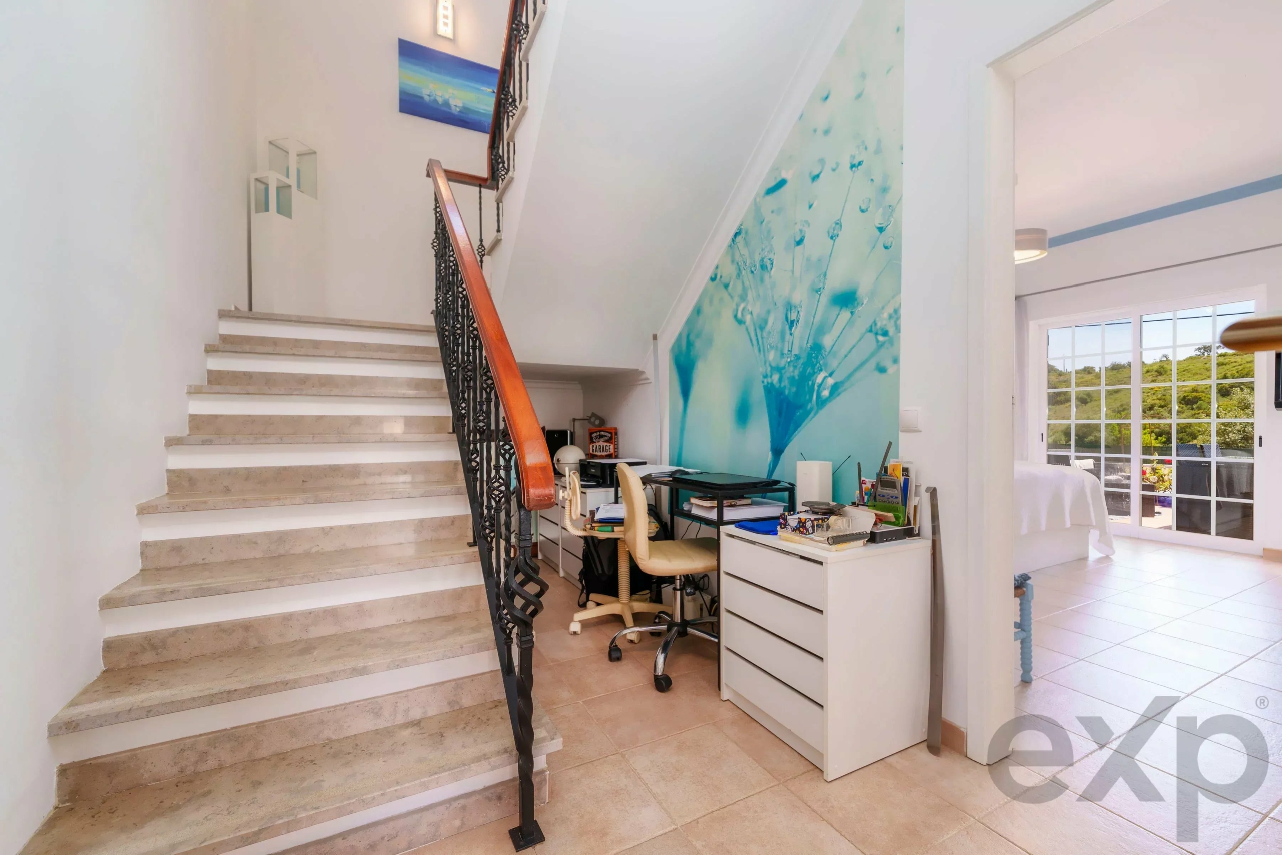 Bright two-story foyer with marble stairs, wrought-iron railing, and a blue wall mural by the staircase.