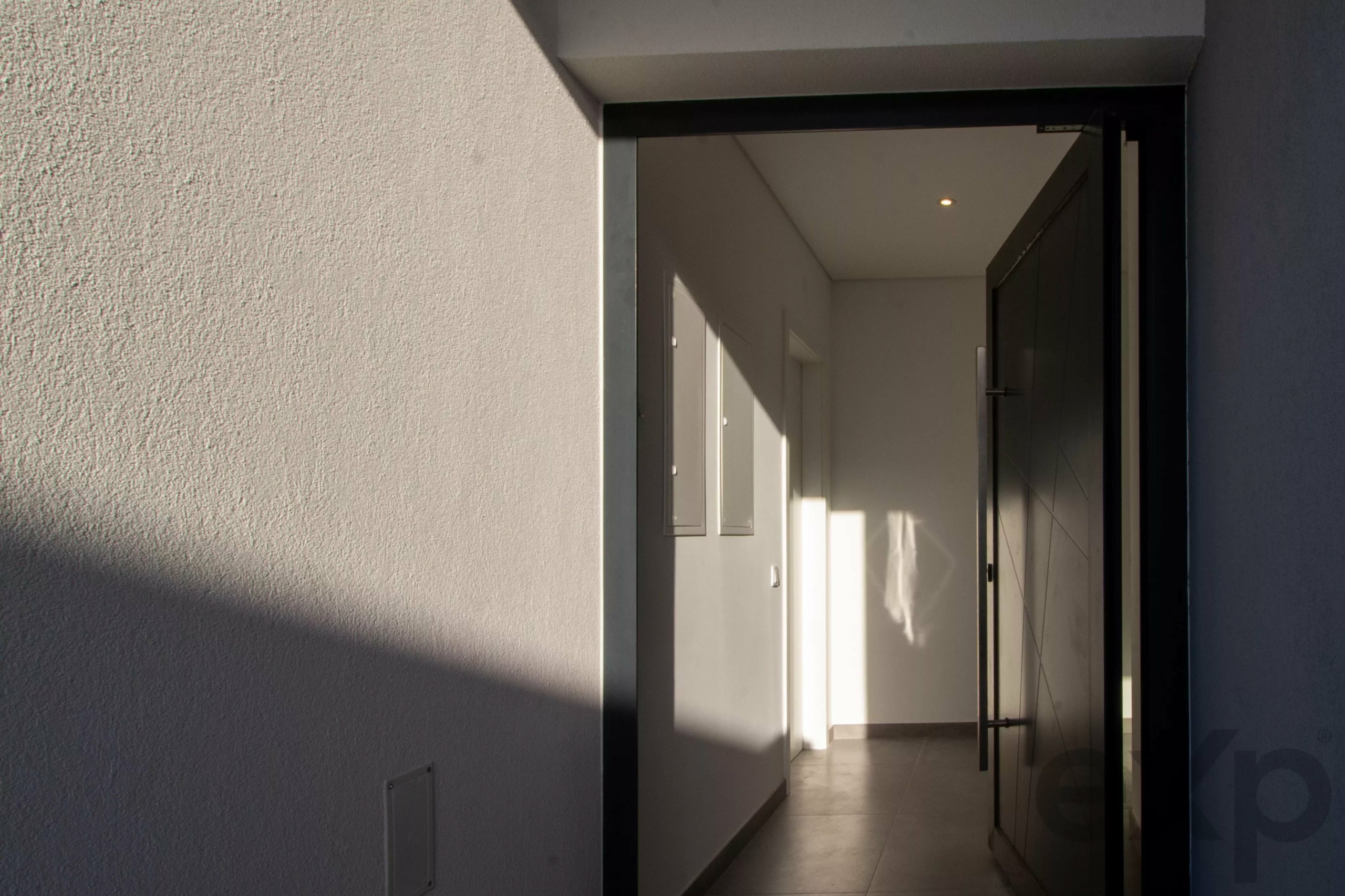Open doorway to a bright white hallway with a tiled floor and a small ceiling light.”?