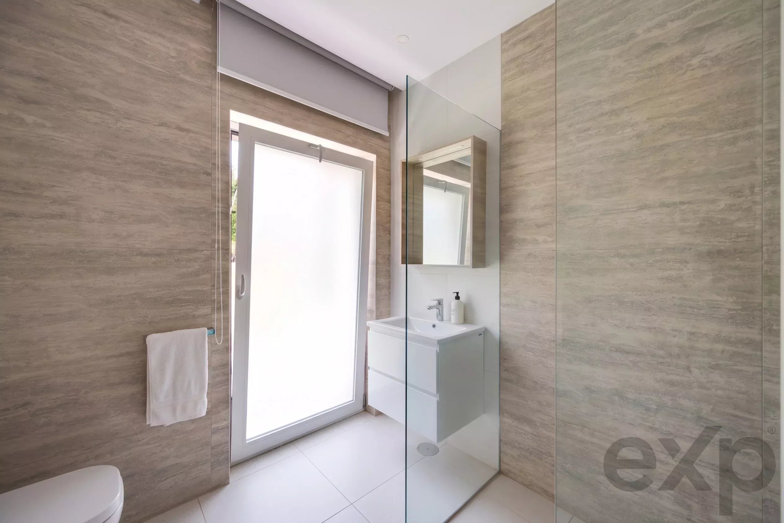 Modern bathroom with a frameless glass shower, white vanity, and beige tiled walls.
