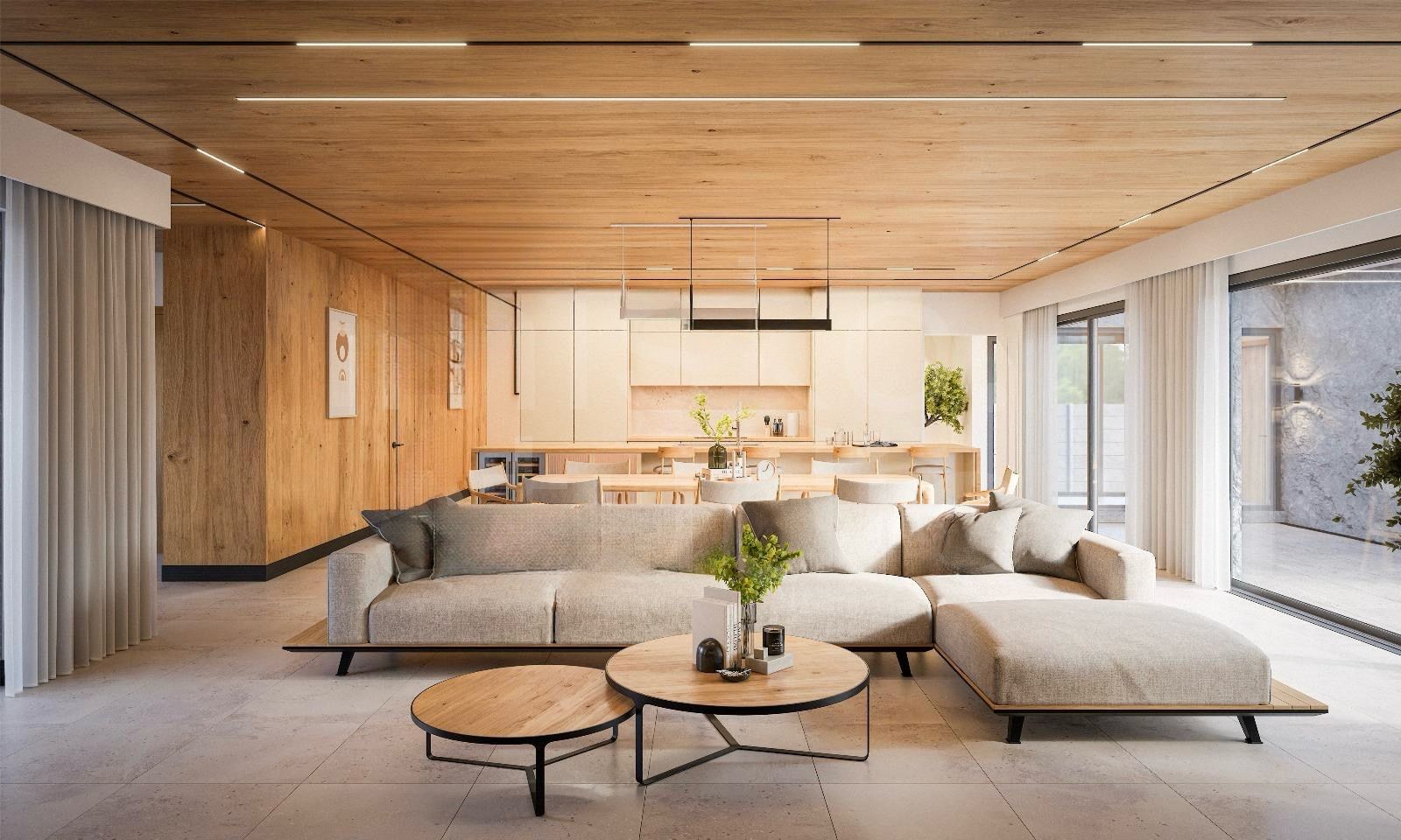 Open living area with a beige L-shaped sofa, round wooden coffee tables, and a white minimalist kitchen at the back.