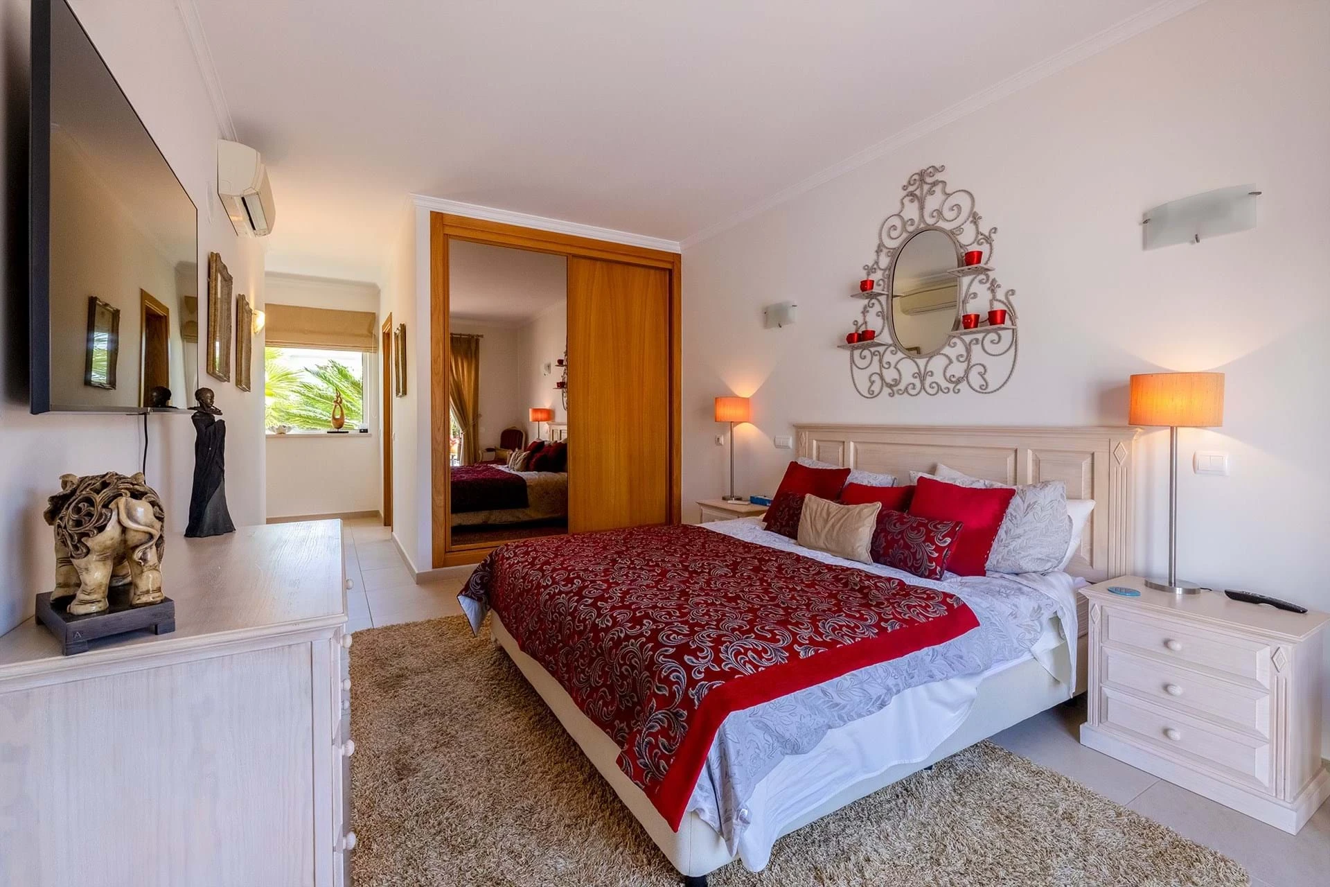 T5 Villa with pool in Ferrel 5mn from beach and Lagos centre – SunnySteve 21 Bright hotel-style bedroom with white furniture, red patterned bedding, and an ornate wall mirror above the headboard.