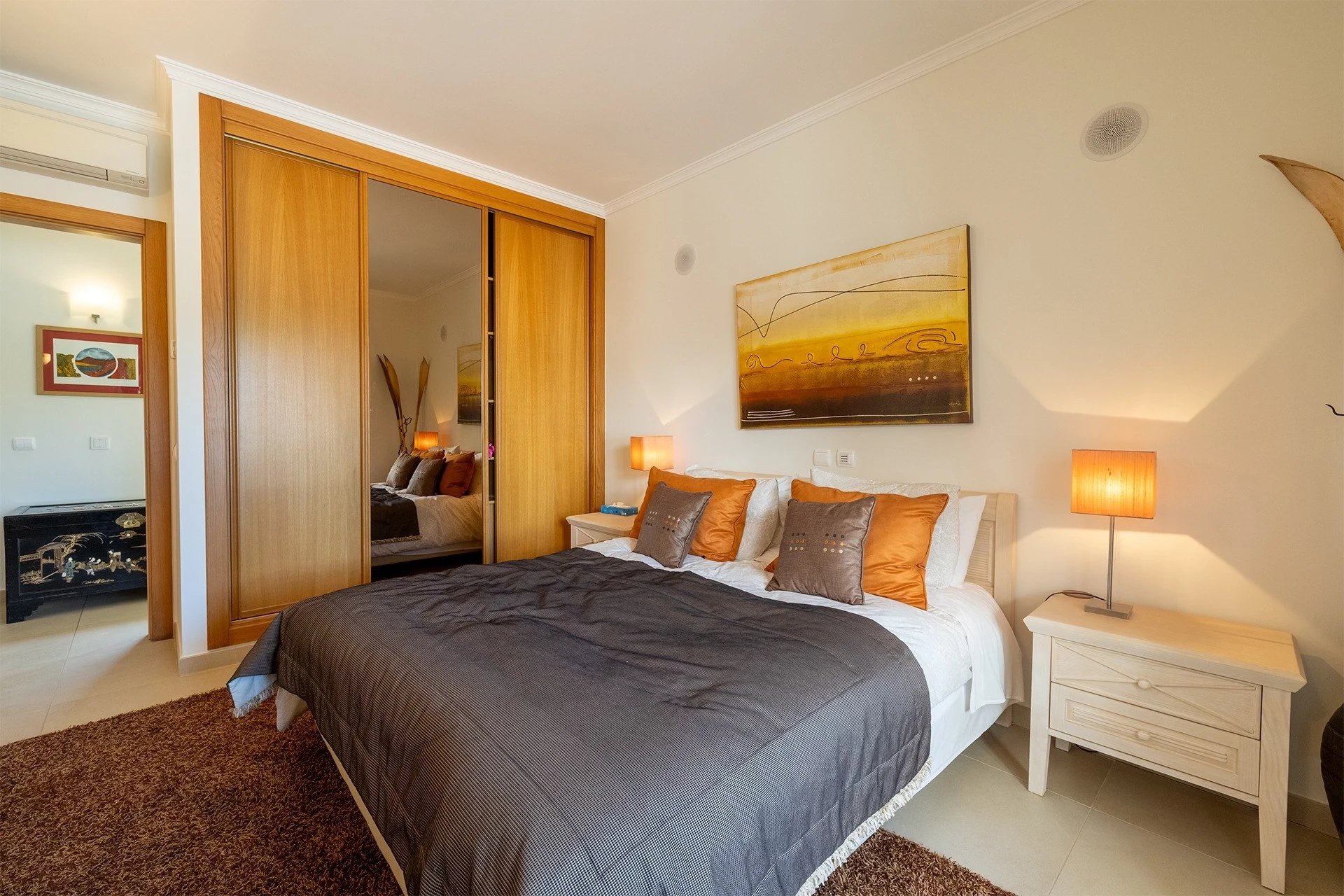 T5 Villa with pool in Ferrel 5mn from beach and Lagos centre – SunnySteve 23 Bedroom with a king bed, dark gray comforter, orange and gray pillows, white nightstands, and a large wooden wardrobe.