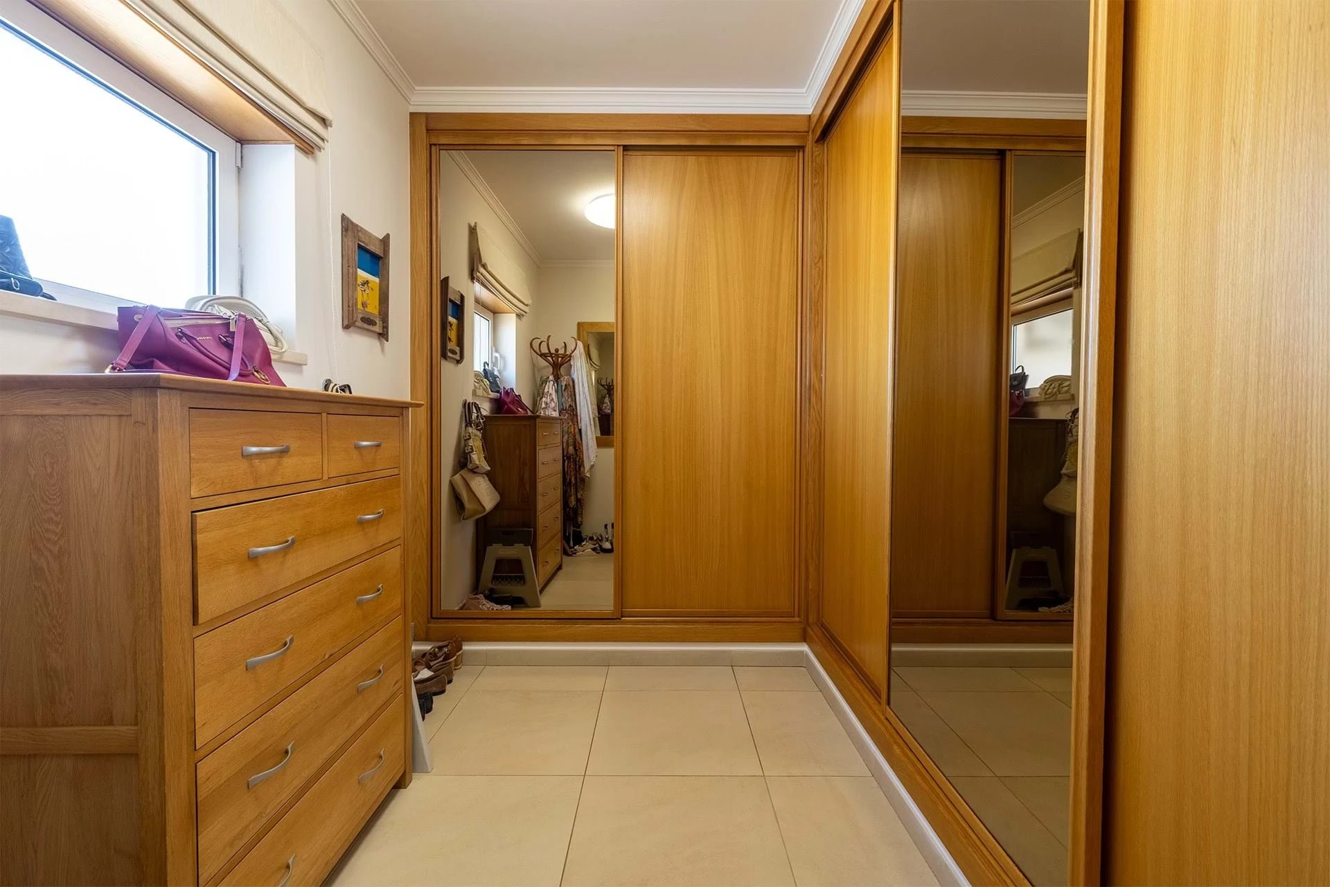 T5 Villa with pool in Ferrel 5mn from beach and Lagos centre – SunnySteve 38 Walk-in closet with wooden wardrobes, a matching dresser, and a large mirror reflecting coats and bags on the back wall.