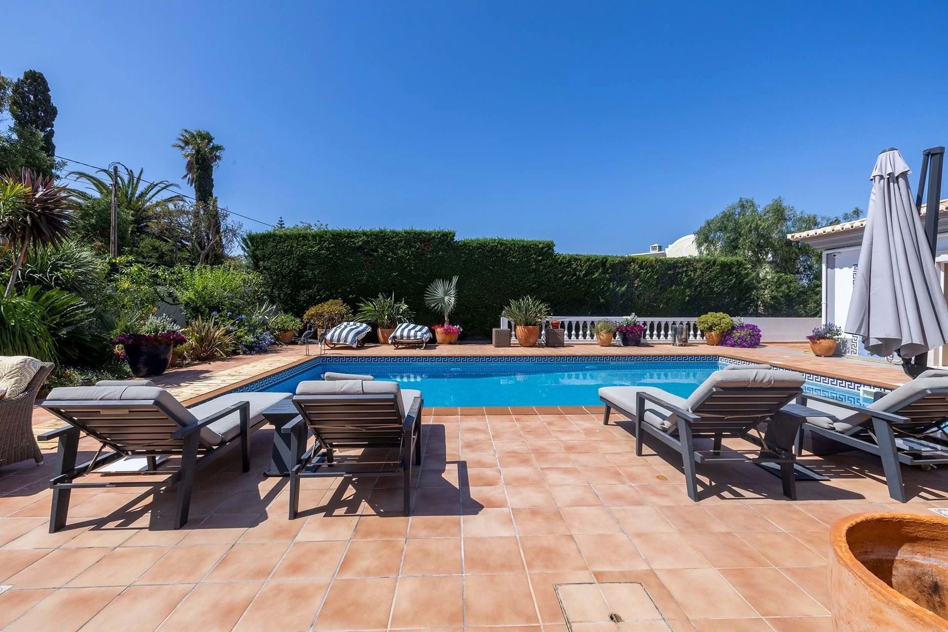 T5 Villa with pool in Ferrel 5mn from beach and Lagos centre – SunnySteve 48 Poolside terrace with lounge chairs, potted plants, and a white umbrella against a clear blue sky.