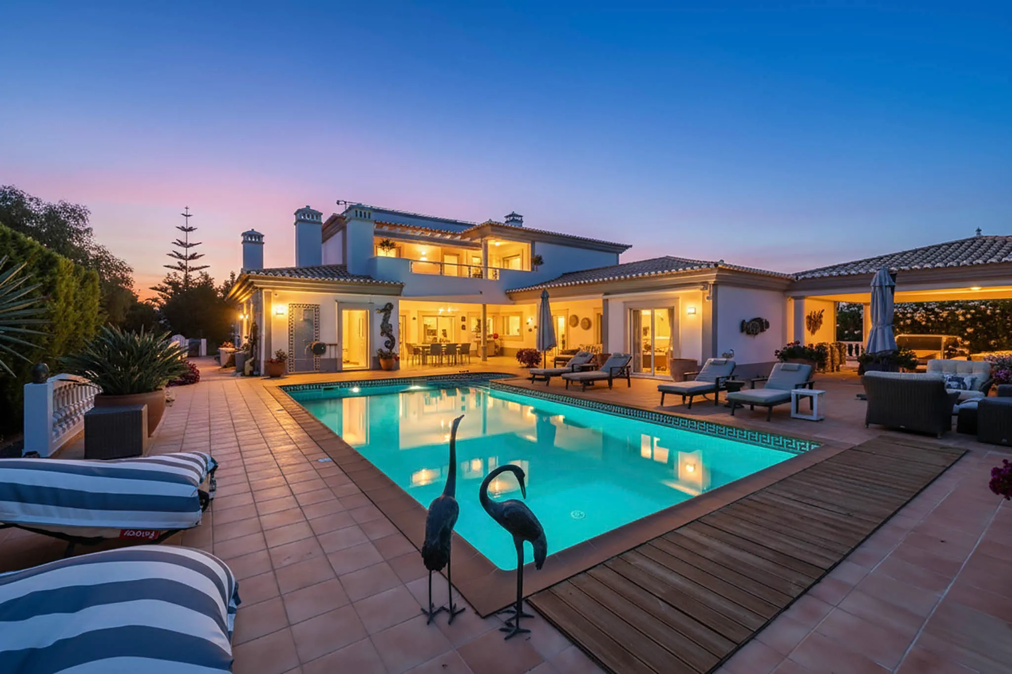 T5 Villa with pool in Ferrel 5mn from beach and Lagos centre – SunnySteve 57 Luxurious white villa with a lit interior, outdoor seating, and a turquoise pool at dusk.