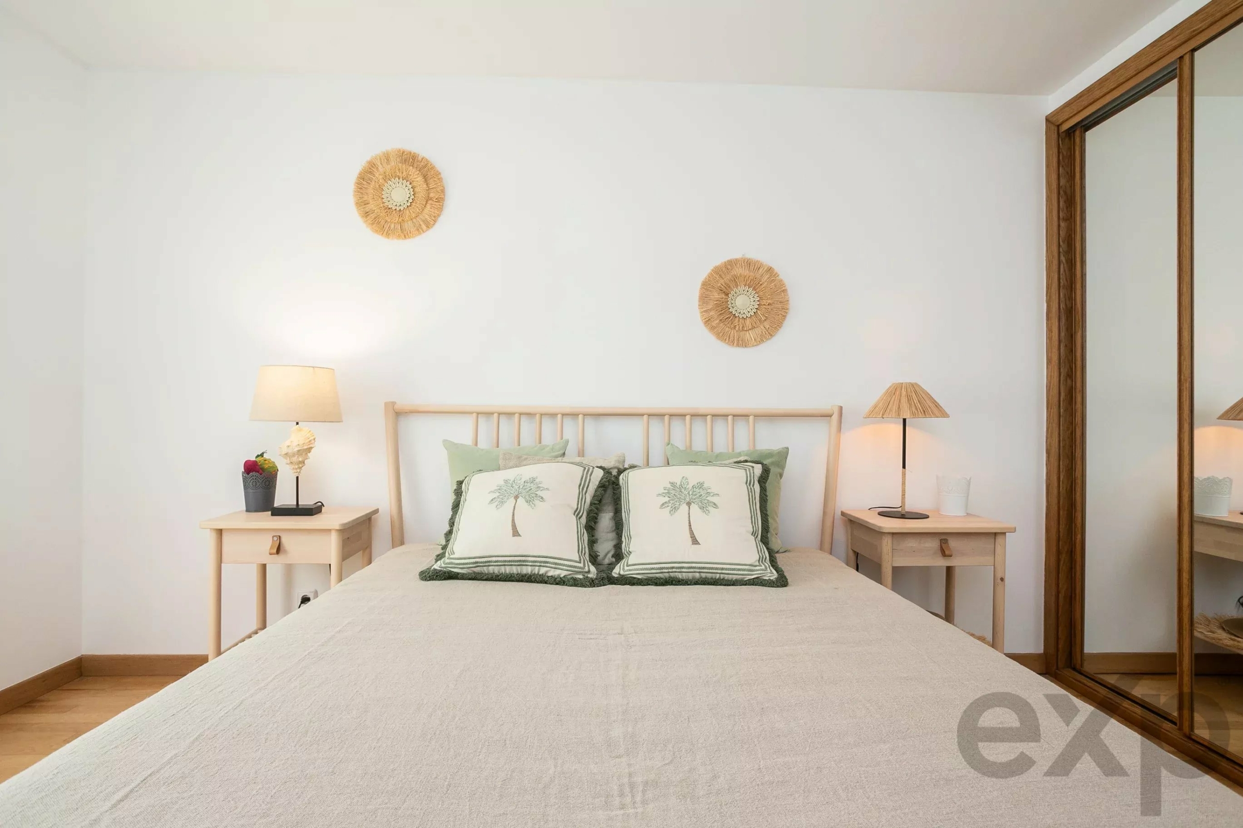 Bright bedroom with a wooden bed, two nightstands, matching lamps, and palm-tree pillows on a light bedspread.