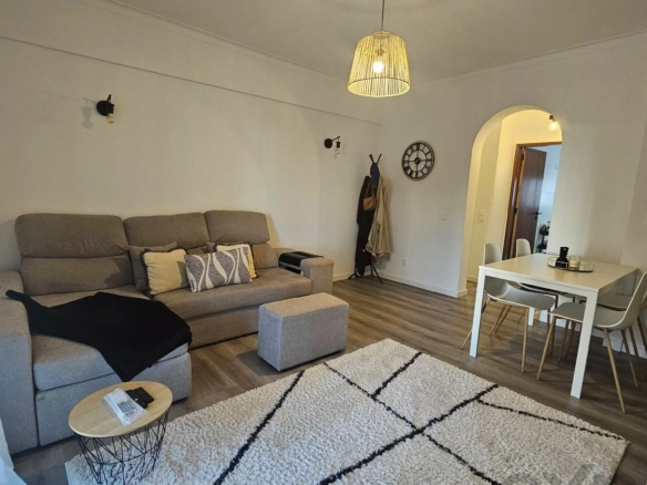 Living room with a gray sectional sofa, a cream rug with black stripes, and a light pendant lamp over a dining area in a modern home interior.