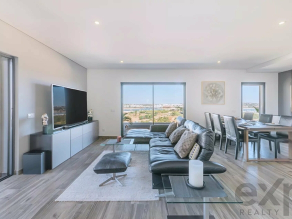 Modern living room with gray sectional, TV on a white cabinet, and a seaside view through large sliding doors