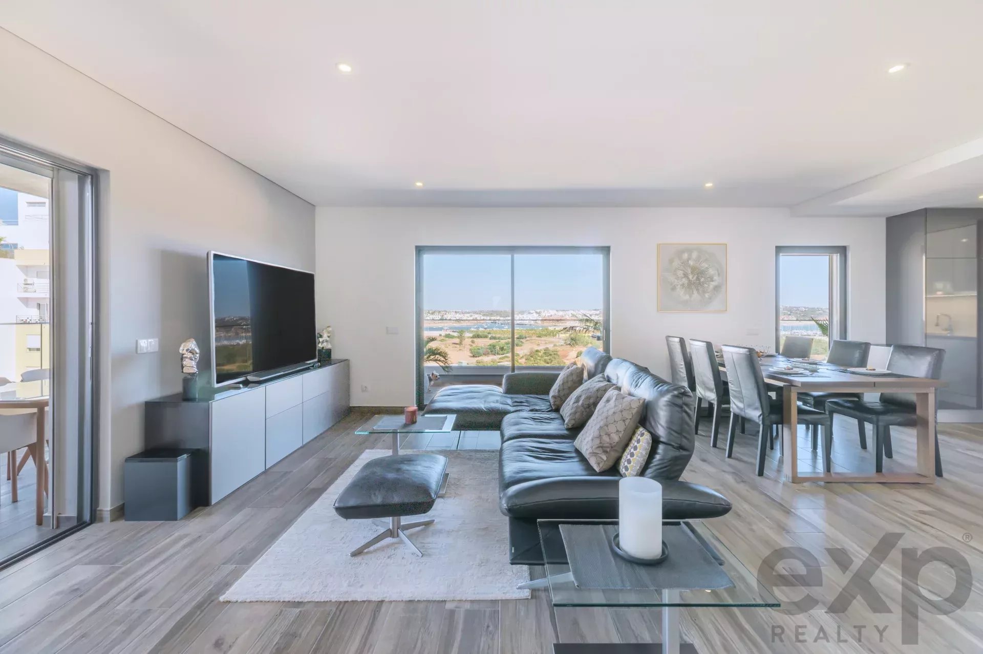 Modern living room with gray sectional, TV on a white cabinet, and a seaside view through large sliding doors