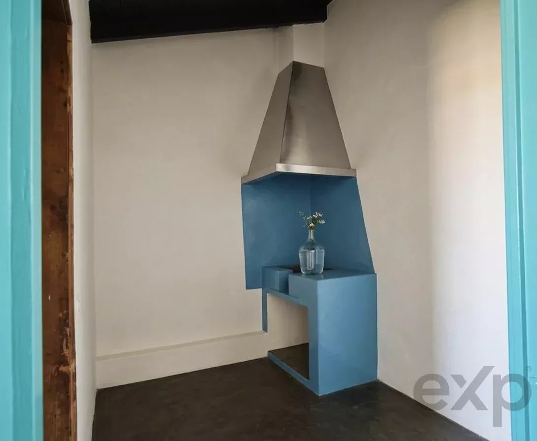 Blue geometric fireplace surround with a stainless steel hood in a small room; a vase with flowers sits on the mantel-like ledge.