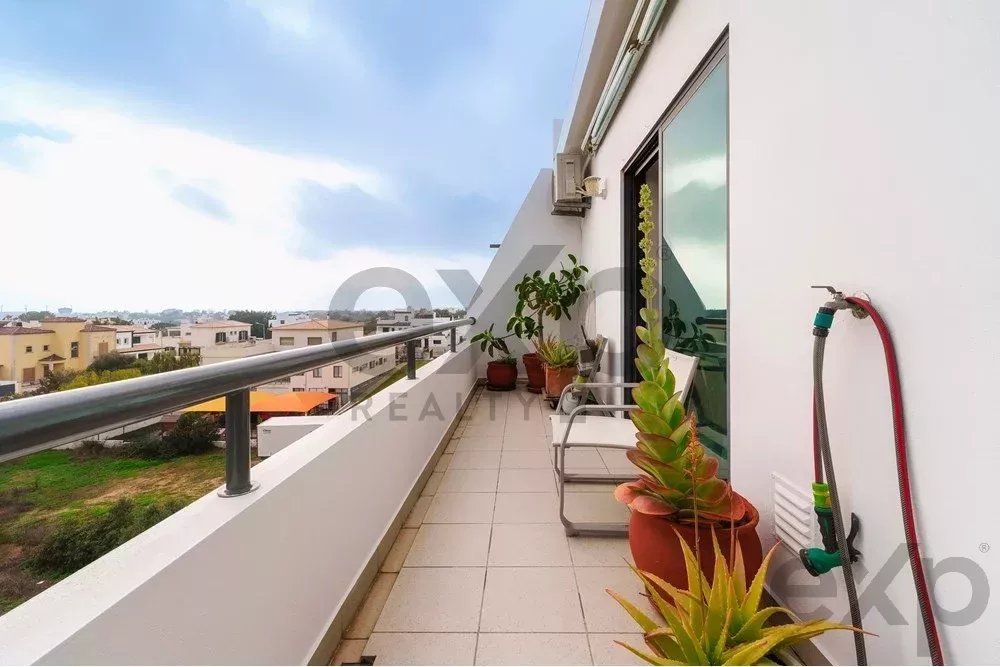 Balcony overlooking a residential area with potted plants, a small chair, and a garden hose attached to the wall.