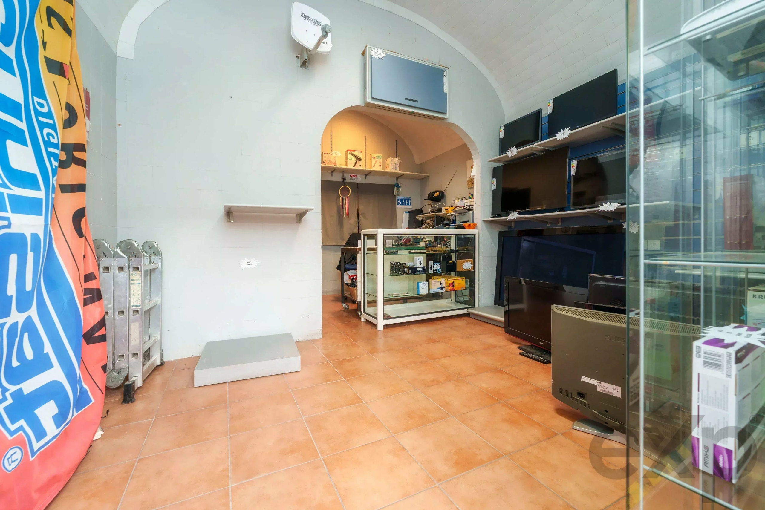 Electronics store interior with large flat-screen TVs on shelves and a glass display case near a curved archway.