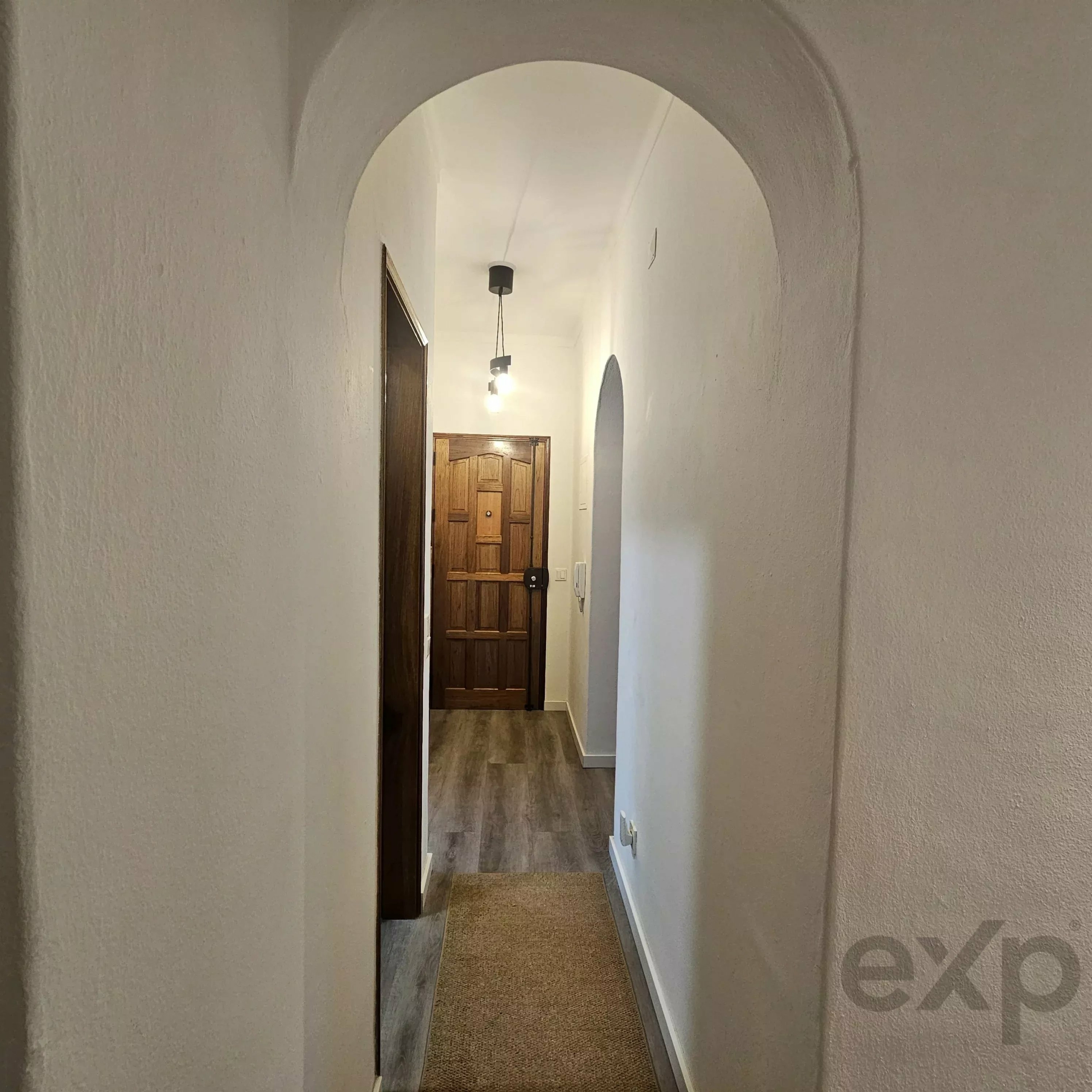 Narrow hallway with arched ceiling leading to a wooden door, illuminated by small hanging pendant lights.