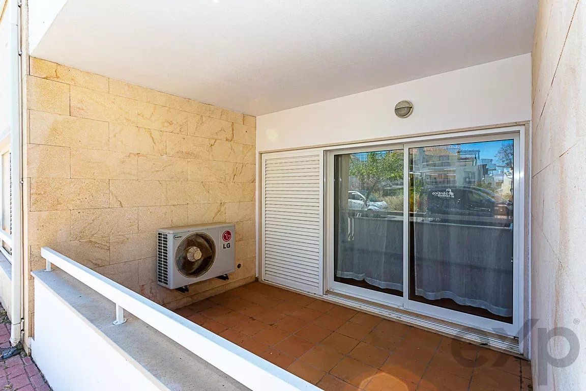 Balcony with beige stone wall, sliding glass door, and an LG outdoor air conditioner unit mounted on the wall above a terra‑cotta tiled floor.